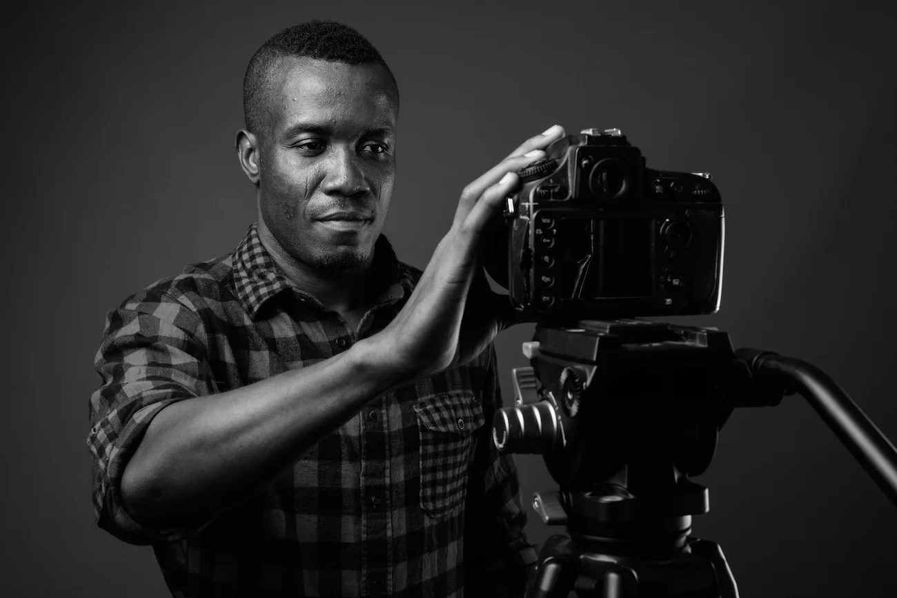 young african man vlogging while wearing checkered shirt against gray wall black white - Stracct Marketing Solutions - Crafting Brands That Build Legacies